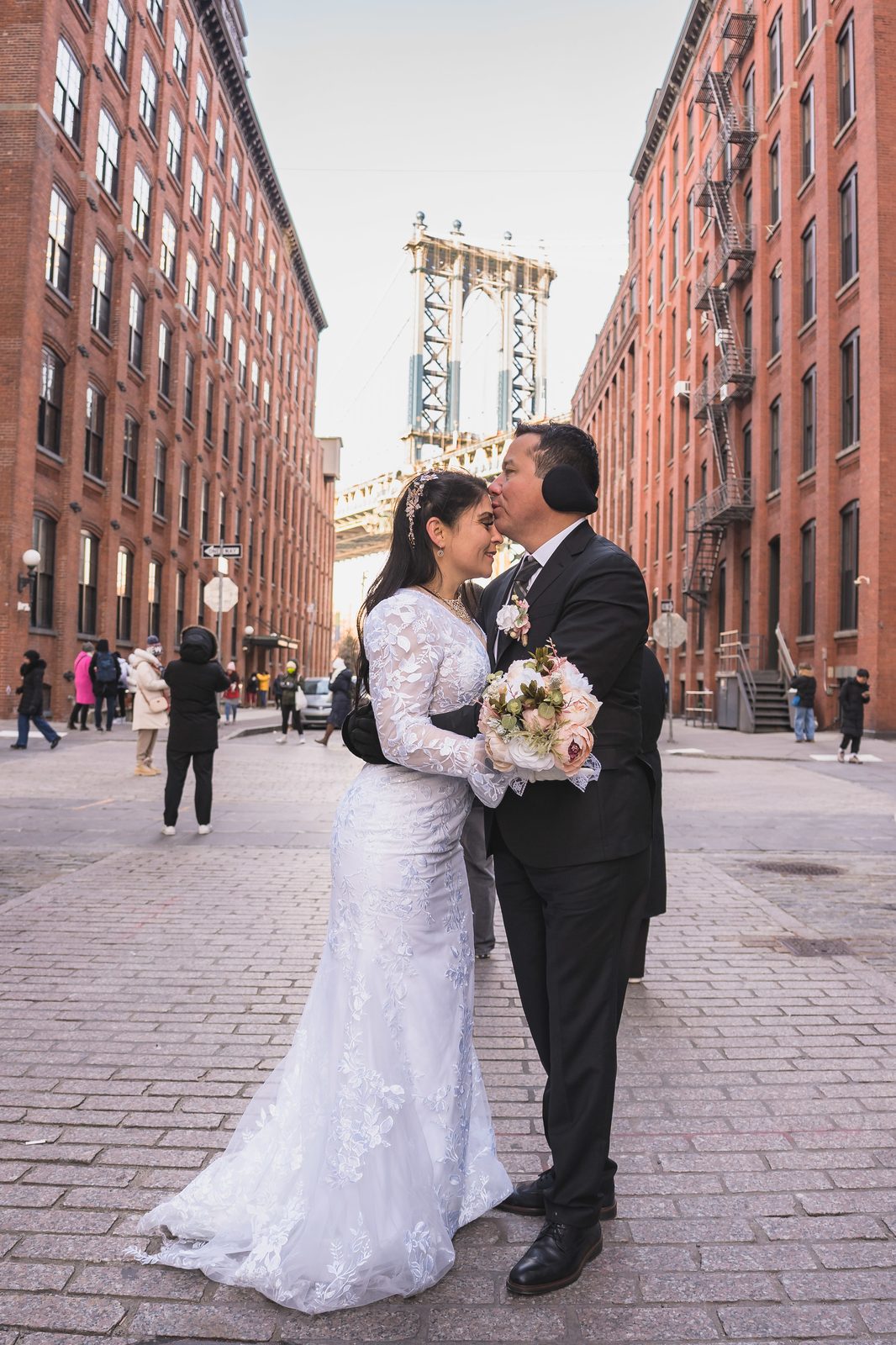 Ana and Mario kissing on a DUMBO cobblestone street with the bridge behind them