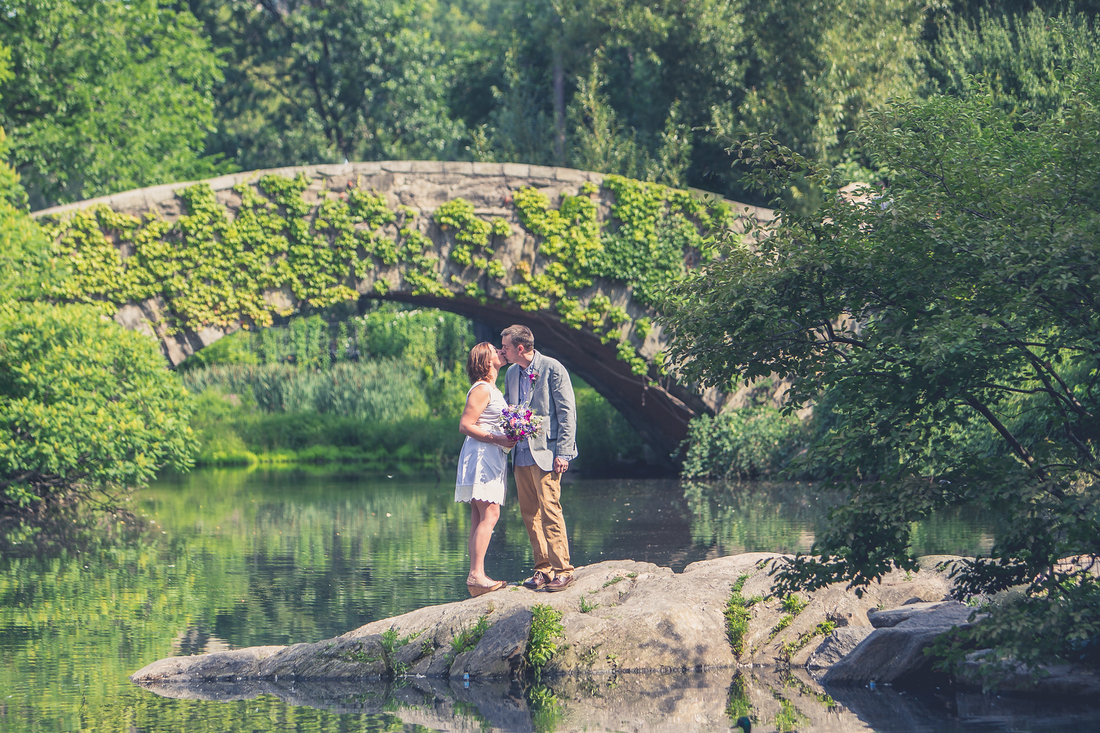 Couple on the rocks by The Pond with Gapstow Bridge behind - Central Park Wedding - New York City